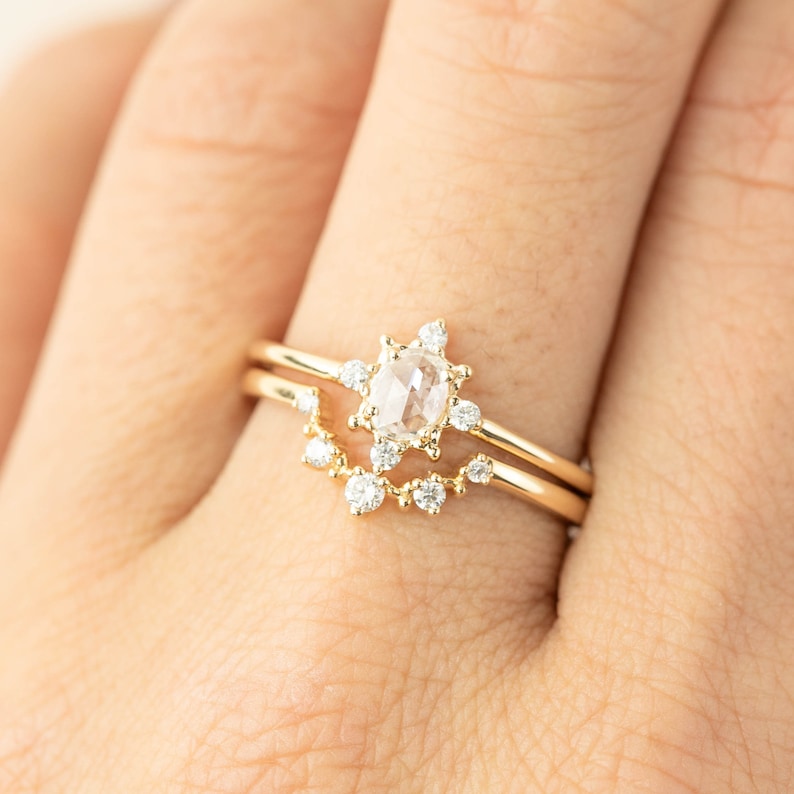 May include: A delicate gold ring set with a round, clear, rose-cut diamond surrounded by smaller diamonds. The ring is worn on a finger.