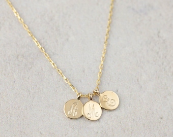 May include: A gold chain necklace with three small round charms, each engraved with a different letter: A, M, and E.