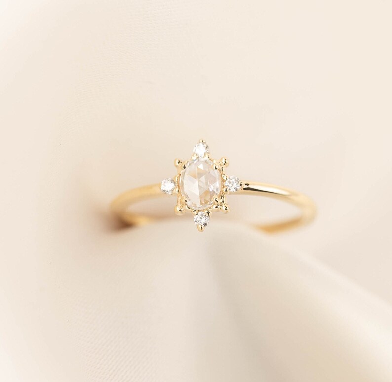 May include: A gold ring with a round, clear gemstone surrounded by smaller diamonds. The ring is set on a white background.