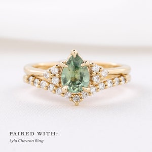 May include: A gold engagement ring with a pear-shaped green gemstone, surrounded by small white diamonds. The ring is paired with a gold chevron ring, also adorned with small white diamonds. Text on the image reads "PAIRED WITH: Lyla Chevron Ring."
