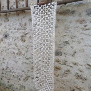 May include: A white crocheted lace tablecloth hanging on a wooden ladder against a stone wall.