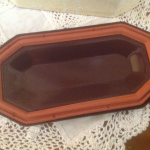 May include: A terracotta-colored rectangular dish with a slightly rounded edge. The dish has a dark brown glaze inside and a smooth, glossy finish.
