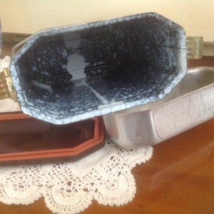 May include: A vintage metal baking dish with a speckled white and black enamel interior. The dish has a removable lid with a metal handle.