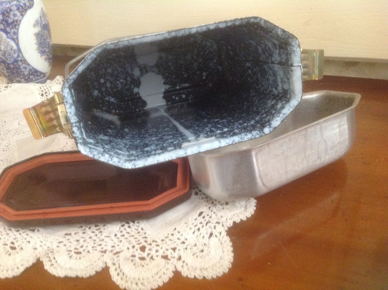 May include: A vintage metal baking dish with a speckled white and black enamel interior. The dish has a removable lid with a metal handle.