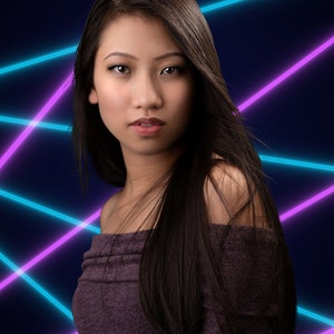 May include: A woman with long dark hair wearing a purple off-the-shoulder top stands in front of a background of blue and purple neon lights.