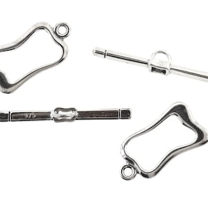 Op de afbeelding: Vier zilverkleurige toggle-sluitingen, een sieradencomponent, worden getoond tegen een witte achtergrond. Twee sluitingen hebben een gebogen, open frame-ontwerp, terwijl de andere twee rechte staven zijn met een sluitmechanisme. Eén staaf is gestempeld met "925".