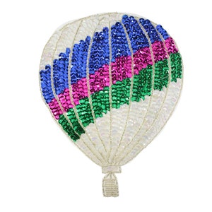 Puede incluir: Un globo aerostático blanco con un diseño colorido de lentejuelas azules, rosas y verdes. El globo tiene una cesta blanca y una cuerda blanca.