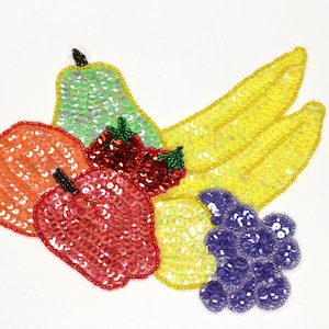 May include: A colourful fruit applique made of sequins. The applique features a pear, two apples, a banana, and grapes. The fruit is arranged in a cluster and is a vibrant mix of red, orange, yellow, green, and purple.