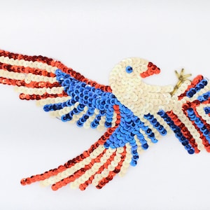 May include: A red, white, and blue sequined eagle with outstretched wings. The eagle is made of small, round sequins and is a patriotic design.