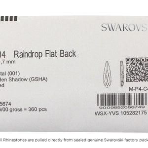 May include: A close-up of a Swarovski Raindrop Flat Back crystal, size 6 x 1.7 mm, in the color Golden Shadow (GSHA). The crystal is foiled and has a barcode and QR code on the label.
