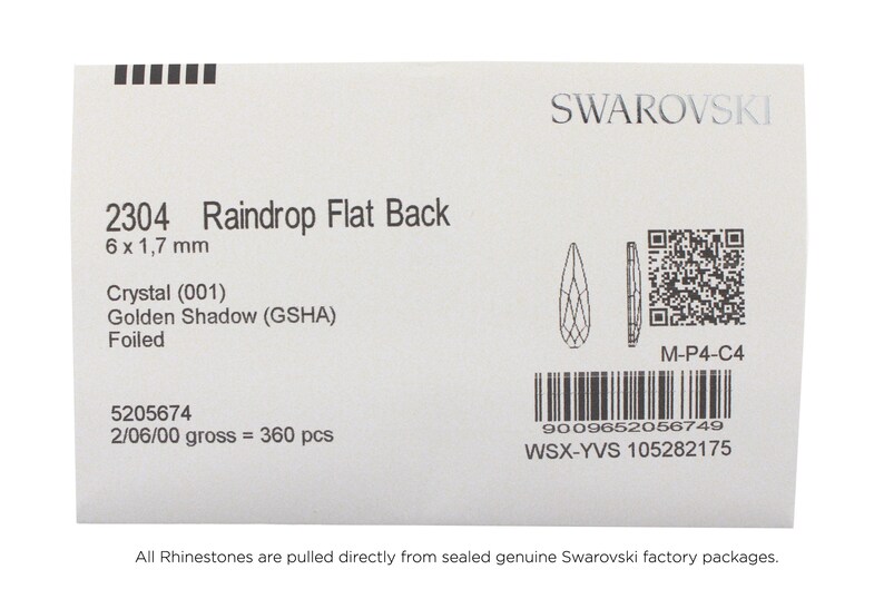 May include: A close-up of a Swarovski Raindrop Flat Back crystal, size 6 x 1.7 mm, in the color Golden Shadow (GSHA). The crystal is foiled and has a barcode and QR code on the label.