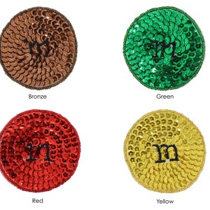May include: Four sequined patches in bronze, green, red, and yellow. Each circular patch features a black letter "m" in the center. The patches are labeled "Bronze", "Green", "Red", and "Yellow".