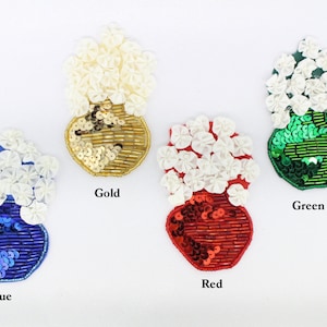 May include: Four embroidered flower vase patches in blue, red, green, and gold. Each patch features a white flower bouquet and a vase with sequins.