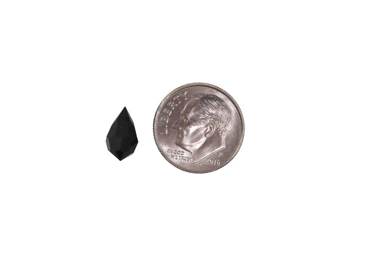 May include: A black faceted teardrop-shaped crystal pendant, approximately the size of a US dime.