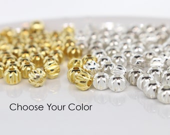 May include: Two piles of small, round beads. One pile is gold and the other is silver. The beads have a textured surface. Choose Your Color.