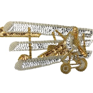 以下が含まれることがあります： 金色と銀色のスパンコールでできた飛行機のアップリケ。飛行機はプロペラと車輪が付いています。このアップリケは、どんなプロジェクトにもヴィンテージな魅力を加えるのに最適です。