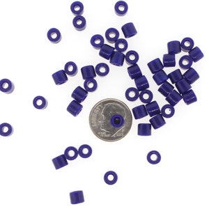 May include: A pile of small, dark purple plastic beads, scattered on a white surface. A US dime coin is included for scale.