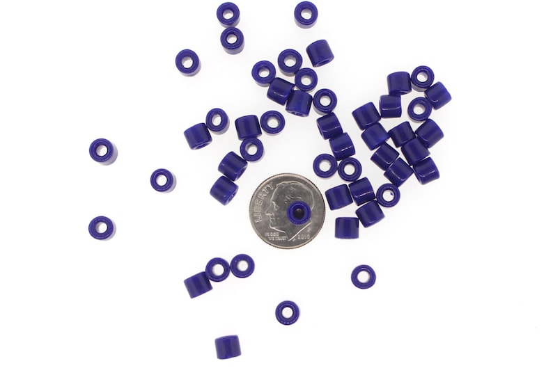 May include: A pile of small, dark purple plastic beads, scattered on a white surface. A US dime coin is included for scale.