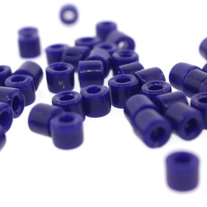 May include: A pile of small, dark blue, round beads. The beads are made of plastic and have a smooth, glossy finish.