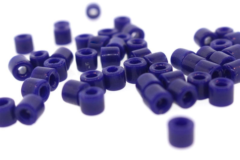 May include: A pile of small, dark blue, round beads. The beads are made of plastic and have a smooth, glossy finish.