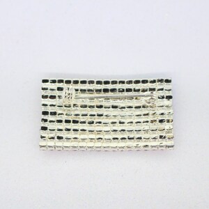Puede incluir: Un broche plateado de forma rectangular con un pasador en la parte posterior. El broche est&aacute; hecho de peque&ntilde;os diamantes de imitaci&oacute;n cuadrados.