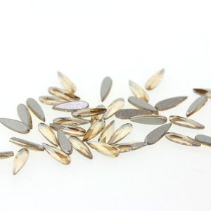 May include: A scattering of small, teardrop-shaped rhinestones in a light gold color. The rhinestones have a slightly iridescent finish.