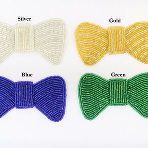 May include: Four beaded bow tie shapes in different colours: silver, gold, blue and green.