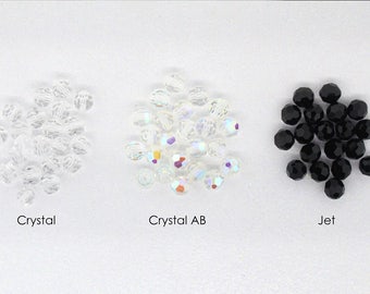 May include: Three piles of round glass beads. The first pile is clear crystal beads. The second pile is iridescent crystal AB beads. The third pile is black jet beads.