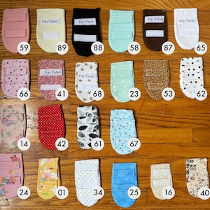 Könnte beinhalten: Eine Sammlung von 16 Stoff-Fingerpuppen mit verschiedenen Mustern und Farben. Die Puppen haben ein Etikett mit dem Text "Pips Petals" und eine Nummer auf jeder.