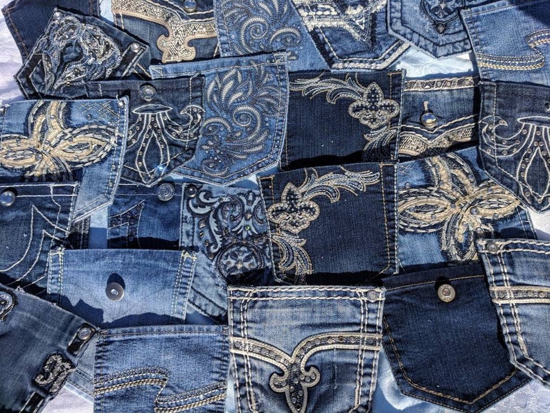 Puede incluir: Una colecci&oacute;n de bolsillos de jeans de mezclilla con varios dise&ntilde;os bordados, que incluyen patrones florales, remolinos y flores de lis. Los bolsillos son de diferentes tonos de azul y tienen una variedad de adornos, como pedrer&iacute;a y cuentas.