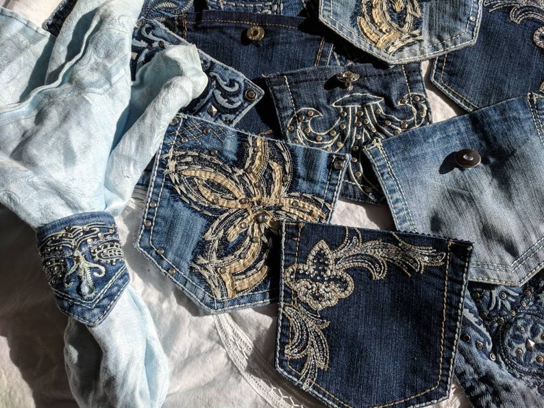Puede incluir: Una colecci&oacute;n de bolsillos de mezclilla con intrincados dise&ntilde;os bordados que presentan patrones florales y de desplazamiento. Los bolsillos est&aacute;n decorados con diamantes de imitaci&oacute;n y cuentas, agregando un toque de brillo y glamour.