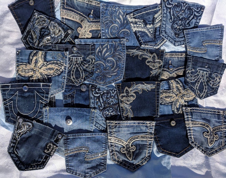 Puede incluir: Una colecci&oacute;n de bolsillos de jeans de mezclilla con varios dise&ntilde;os bordados. Los bolsillos son en tonos de azul y presentan patrones intrincados con pedrer&iacute;a y lentejuelas.