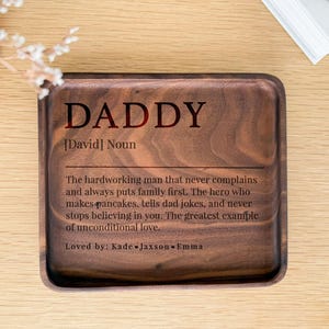 May include: A wooden tray with the word "DADDY" in large, dark letters. The tray includes a definition of "Daddy" and is inscribed with the words "Loved by: Kade Jaxson Emma."