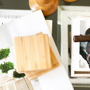 May include: A set of four natural bamboo coasters stacked on top of each other. The coasters are square and have a smooth, polished surface.