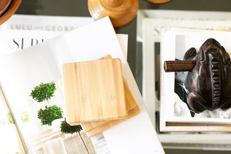 May include: A set of four natural bamboo coasters stacked on top of each other. The coasters are square and have a smooth, polished surface.