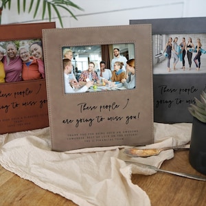 May include: Three photo albums in brown, tan, and gray, each with a framed photo and the text "These people are going to miss you!" The albums are on a light-colored surface with a plant and silverware.