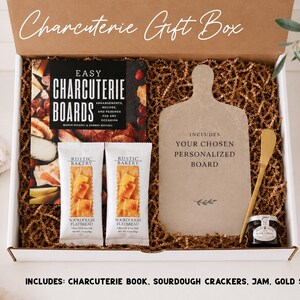 a gift box containing a variety of items, including a book, a sourdough cracker, a jar of jam, and a gold spreader. The box is labeled as a "Charcuterie Gift Box" and includes a sourdough cracker, a jar of jam, and a gold spreader.