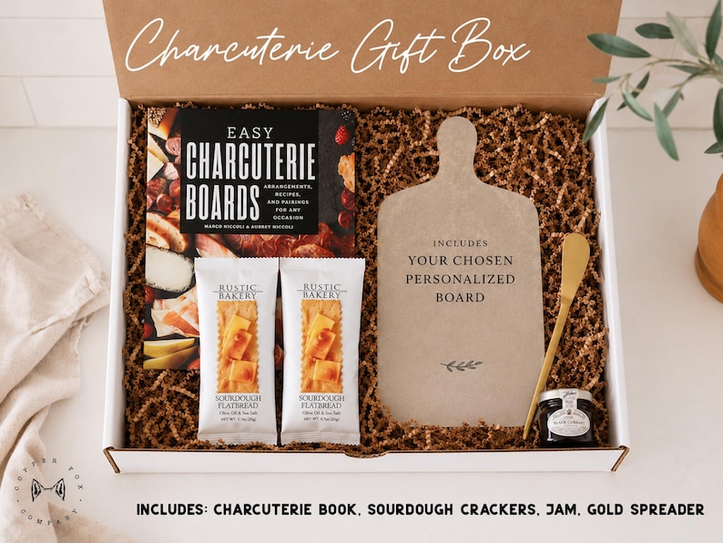 a gift box containing a variety of items, including a book, a sourdough cracker, a jar of jam, and a gold spreader. The box is labeled as a "Charcuterie Gift Box" and includes a sourdough cracker, a jar of jam, and a gold spreader.