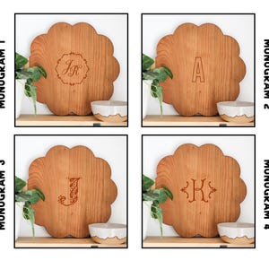 May include: Four wooden serving trays with different monogram designs. The trays are round with a scalloped edge and are made of light brown wood. The monograms are in a classic font and are engraved in a darker brown color. The monograms are "JR", "A", "J", and "KH".