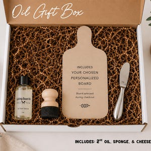 a gift box containing various items, including a cutting board, a bottle of oil, a sponge, and a cheese knife. The box is open, revealing the contents inside.
