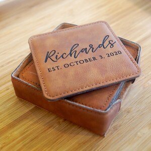 May include: Set of brown leather coasters with stitched edges. The top coaster has the text "Richards EST. OCTOBER 3, 2020" engraved in black.
