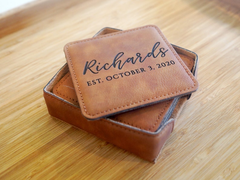 May include: Set of brown leather coasters with stitched edges. The top coaster has the text "Richards EST. OCTOBER 3, 2020" engraved in black.