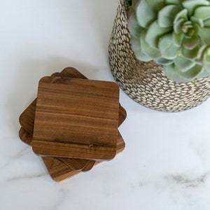 May include: Four brown wooden coasters stacked on top of each other on a white marble surface.