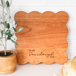 May include: A wooden cutting board with a scalloped edge and the text "In My Sourdough Era" engraved on the surface.