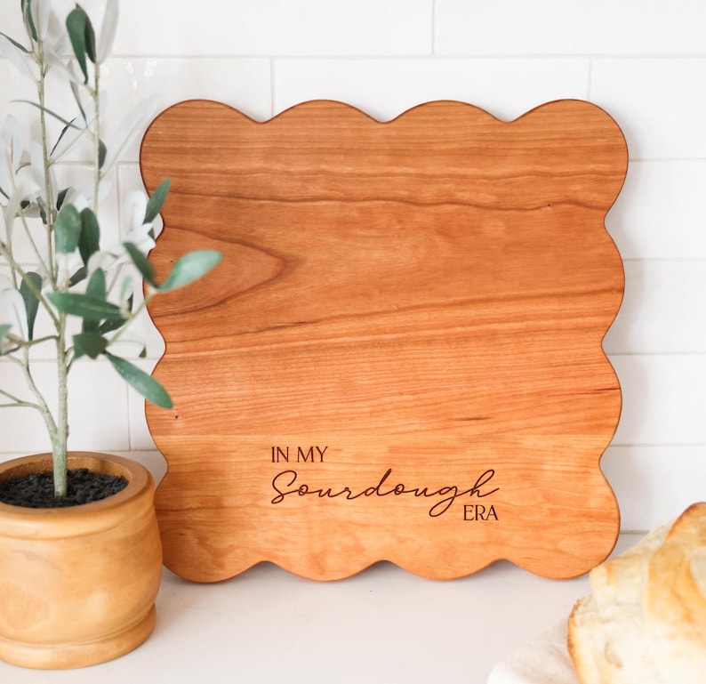 May include: A wooden cutting board with a scalloped edge and the text "In My Sourdough Era" engraved on the surface.