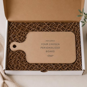 a cardboard box containing a wooden cutting board, with a potted plant and a cloth visible in the background.