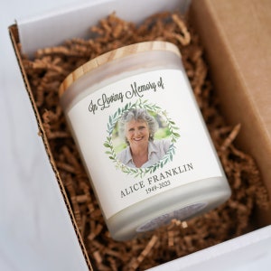 K&ouml;nnte beinhalten: Eine wei&szlig;e Kerze mit einem Holzdeckel, die ein Foto einer Frau mit einem Blumengirlanden zeigt. Der Text "In Loving Memory of Alice Franklin 1949-2023" ist auf die Kerze gedruckt.
