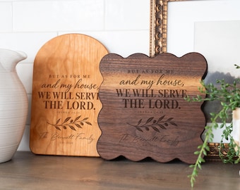 Może przedstawiać: Dwie drewniane tabliczki ścienne z wygrawerowanym tekstem "BUT AS FOR ME and my house, WE WILL SERVE THE LORD. JOSHUA 24:15" oraz "The Bennett Family EST. 2020" z grafiką gałązki oliwnej. Jedna tabliczka jest z jasnego drewna z łukowatym szczytem, druga z ciemnego drewna z falistym brzegiem.