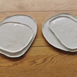 May include: Set of two white ceramic plates with an organic, irregular shape. The plates are nested together, with the smaller plate inside the larger one.