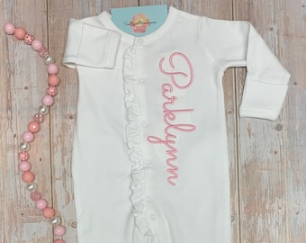 May include: White baby onesie with pink ruffled trim and the name "Parklynn" embroidered in pink.